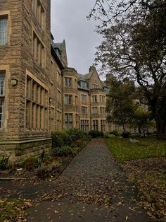 an old stone building with many windows and trees in the front yard on a cloudy day