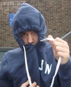 a young man in a hoodie is holding something up to his mouth and looking at the camera