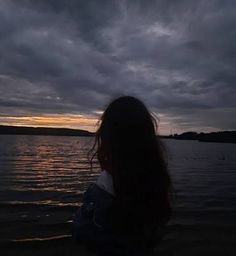 a woman standing in front of a body of water at night with the sun setting