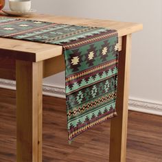 a wooden table topped with a green and brown table runner next to a bowl of fruit