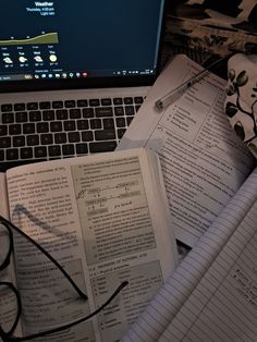 an open laptop computer sitting on top of a desk next to notebooks and papers