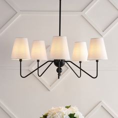 a chandelier with five lamps hanging from it's sides and flowers on the table