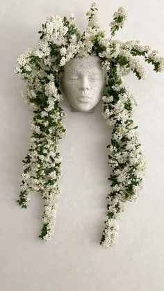 a white head with flowers on it and a wreath around the face that is hanging down