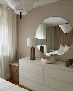 a white dresser topped with a mirror next to a lamp and a large round mirror