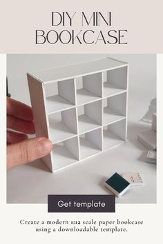 a hand holding a small bookcase next to a pile of books