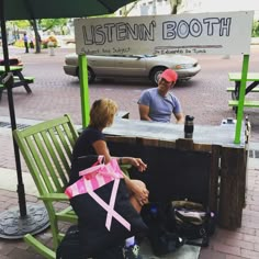 a man and woman sitting at a booth on the sidewalk