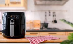 a black air fryer sitting on top of a wooden counter next to a red and white checkered napkin