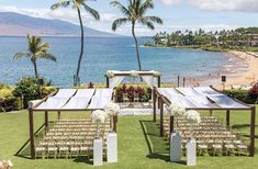 an outdoor wedding set up with chairs and flowers on the grass by the water in front of palm trees