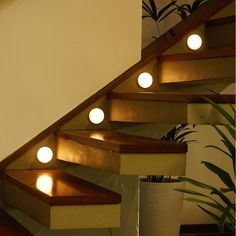 some lights that are on the side of a set of stairs near a plant in a vase