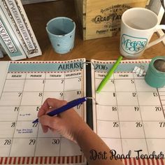 a person writing on a calendar next to coffee mugs