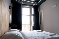 a bed with white sheets and pillows in front of a window that has black curtains