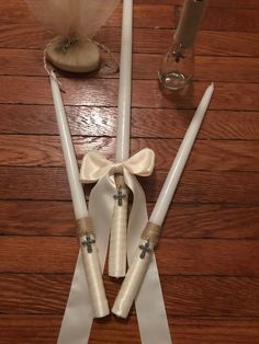 two white candles with bows on them sitting on a wooden table next to some wine glasses