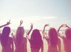 four women standing on the beach with their arms in the air and one woman holding her hands up