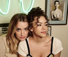 two women sitting next to each other in front of a neon light sign and wall