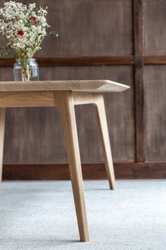 a wooden table sitting on top of a carpeted floor next to a vase filled with flowers