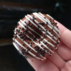 a chocolate donut with white frosting and sprinkles is held in someone's hand