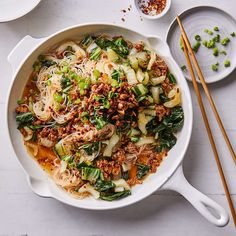 a white bowl filled with noodles and vegetables next to chopsticks on a table