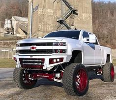 a white truck with red rims parked in front of a large stone building on top of a hill