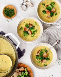 three bowls of soup with broccoli and meat in them on a white table