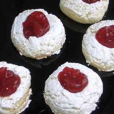 four pastries covered in powdered sugar and jam on top of a black surface