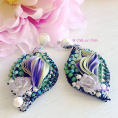 a pair of blue and green beaded earrings next to a pink peonie flower