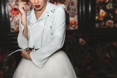 a woman in a white dress and jacket is posing for a photo with her hand on her chin