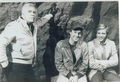 an old black and white photo of three men sitting next to each other in front of rocks