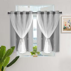 two white curtains hanging on the side of a window next to a potted plant