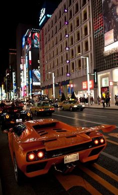 an orange sports car is parked on the side of the road in front of tall buildings