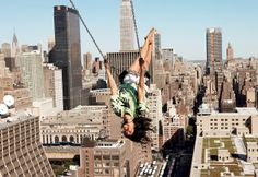 a man hanging upside down from a high building in the middle of a large city