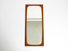 a mirror mounted to the side of a white wall next to a wooden shelf with an object on it