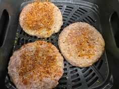 three hamburger patties being cooked in an air frying pan with seasonings on top