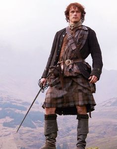 a man dressed in scottish clothing standing on top of a hill