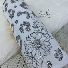 a white vase with black and silver designs on it sitting on a wooden table next to a feather pillow