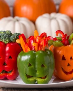 three peppers with faces carved into them on a plate next to pumpkins and broccoli