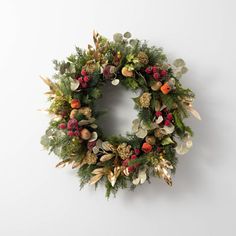 a christmas wreath hanging on the wall in front of a white wall with red berries and greenery