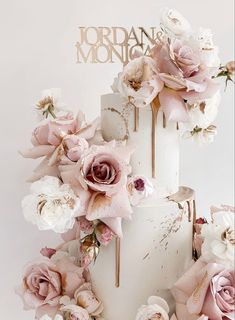 a three tiered cake with pink and white flowers on the top is surrounded by gold lettering