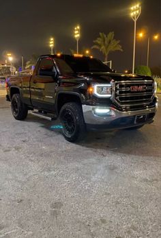 a black truck parked in a parking lot next to street lamps and palm trees at night