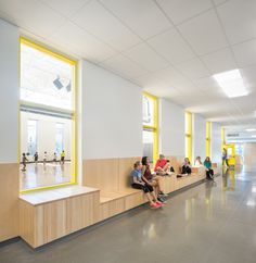 people are sitting on benches in an empty building with bright yellow trim around the windows