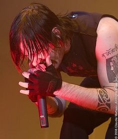 a man with tattoos on his arm holding a microphone in front of his face and looking down