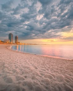 the beach is empty and there are clouds in the sky over the water at sunset