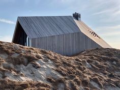 a house on top of a hill with sand and grass in the foreground, under a blue sky