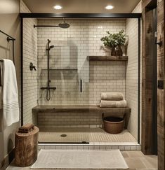 a walk in shower sitting next to a wooden bench and towel rack on the wall