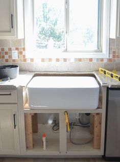 a kitchen sink under a window in front of a dishwasher and cabinets with tools on the counter