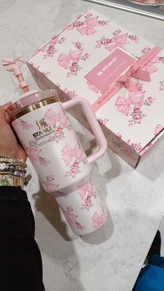 a person is holding a pink coffee mug in front of a box with a bow on it