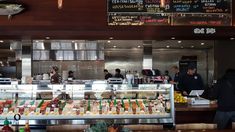 people standing in line at a restaurant with food on the counter and menus hanging above