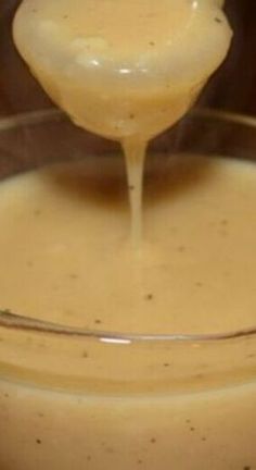 a spoon full of liquid being poured into a glass bowl filled with batter or sauce