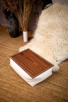 a wooden box sitting on top of a rug next to a vase with dry grass in it