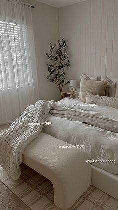 a white bed sitting in a bedroom next to a window with sheer curtains on it