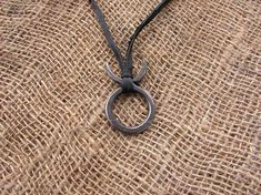 a black necklace with a metal ring hanging from it's side on a burlap surface